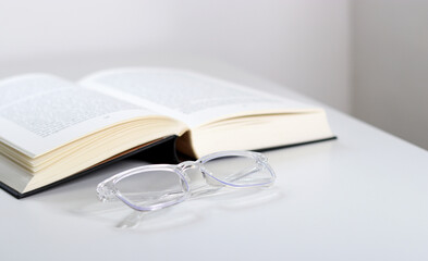Close up of transparent glasses and an open book on white table 