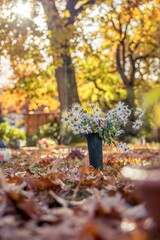 Weiße Blumen stehen auf der Rasenfläche eines Friedhofs. Es ist Herbst, die Sonne scheint und viel Laub ist bereits zu Boden gefallen.