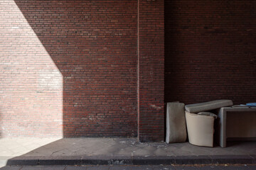 An outdoor scene featuring an abandoned pile of furniture against a weathered red brick wall.