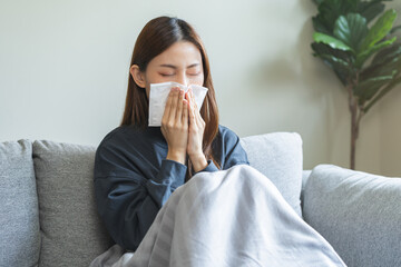 Sick, coronavirus or covid-19, attractive asian young woman, girl have a fever, flu and hand in use tissues paper sneezing nose, runny while sitting on sofa, couch at home. Health care on virus person