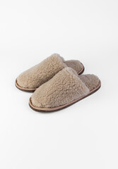 A pair of beige slippers made of natural fur on a white background. View from above