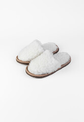 A pair of white slippers made of natural fur on a white background. Place for text