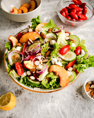 Summer salad with cherry tomatoes, baked pepper, salad mix, peaches, cucumber, and red onion, topped with feta cheese. Keto diet, healthy food. Light grey stone background. Top view.