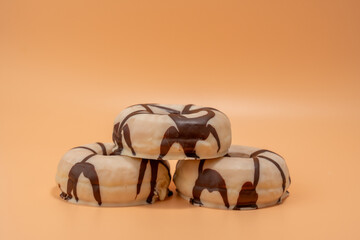 Three donuts stacked on top of each other with chocolate and vanilla frosting. Donuts are located on an orange background.