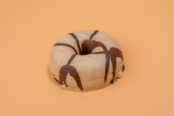 Chocolate covered donut sits on a yellow background close-up.