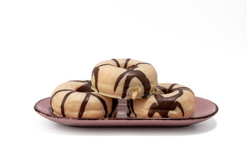 Three donuts with chocolate icing on a pink plate. The plate is on a white background. The donuts are stacked on top of each other