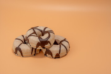 Three donuts with chocolate icing on top. The donuts are stacked on top of each other