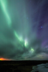Long exposure of the Aurora Borealis above a beach in the Icelandic Westfjords with a starry sky.