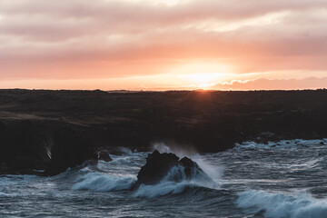 Moody sunset at an Icelandic coast with waves crushing against rocks.