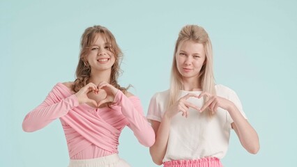 Young fashionable women models show heart gesture, isolated on blue background. Fashion and youth beauty concept.
