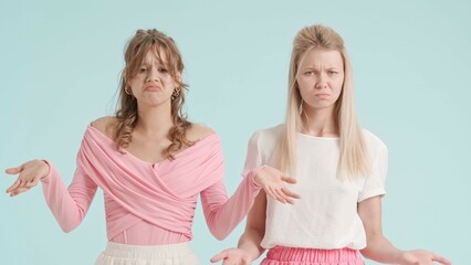 Young fashionable women models shrugging with confused negative expression, isolated on blue background. Fashion and youth beauty concept.