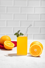 fresh orange juice in a glass with a slice of fruit on a table with a white brick wall as a background. Copy space