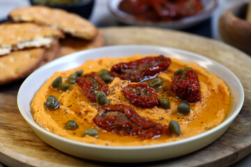 Hummus with sun-dried tomatoes and capers on a plate