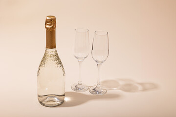 A bottle of white sparkling wine in two glasses on a beige background. Copy space