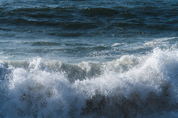 Foaming white ocean waves at the shore close-up, blue water in the background.
