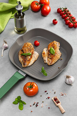 New grill frying pan on the kitchen table with cooked chicken breast and products: cherry tomatoes, salt, oil, spices. Advertising of utensils for cooking.
