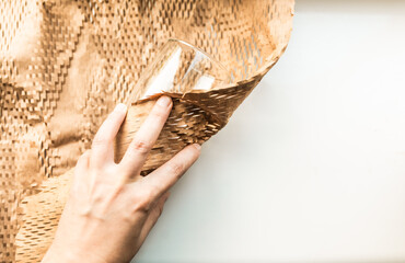 Someone packs a glass into a brown eco friendly packing paper for moving. Packing glass for post delivery.