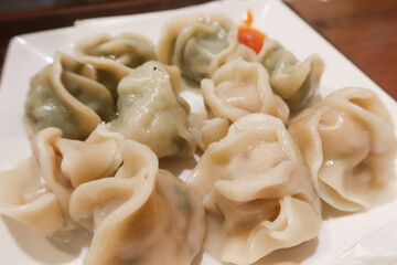 close up of Chinese steamed boiled meat and vegetables pork dumplings on a white plate with spicy chilly sauce at the side