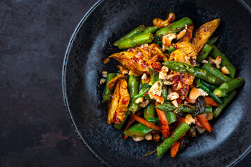 Traditional stir-fried spicy chicken fillet nuggets bowl with green asparagus, cashew nuts and broccoli in sweet sour sauce served as top view  in a design bowl with text space
