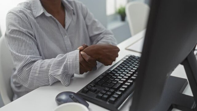 Woman in office holding wrist while sitting at desk with computer suffering pain and discomfort during work