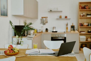 Medium close up of wooden dining table with fruit bowl and laptop in comfort modern kitchen