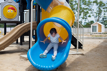 A young girl is sitting on a sky blue slide, smiling and waving. Concept of joy and excitement, as...