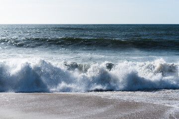 Foaming white ocean waves at the shore close-up, blue water in the background.