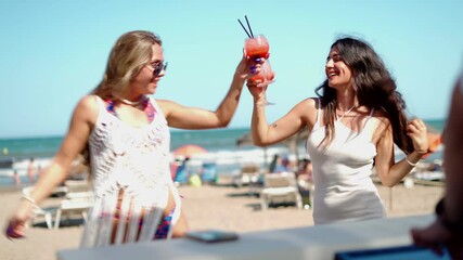 Two women dance on the beach to the music of a DJ, enjoying the summer day and each other's company.