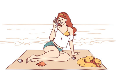 Woman sits on beach and listens to sound of sea from shell, enjoying summer vacation at tropical resort. Tourist girl sunbathes on beach of paradise island in ocean during weekend.