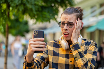 Shocked young man using smartphone typing browsing, loses becoming surprised sudden lottery...