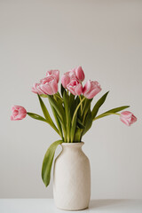 Beautiful pink tulip flowers bouquet in ceramic vase on white table. Aesthetic minimalist style floral composition with copy space