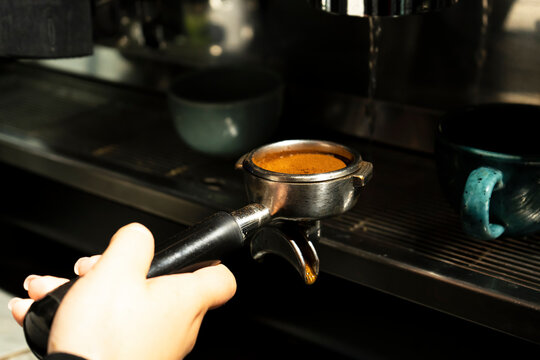 Freshly ground pressed coffee, ready to be served in a professional automatic coffee machine. A woman's hand holds a pre-filter with ground coffee, preparing it for brewing. Process of making espresso