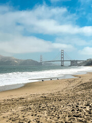 Coastal view of the Golden Gate bridge in San Francisco. American iconic landmark. Cliffs and grass frame the picture. Waves in the bay water. Light fog.