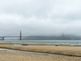 Coastal view of the Golden Gate bridge in San Francisco. American iconic landmark. Cliffs and grass frame the picture. Waves in the bay water. Light fog.
