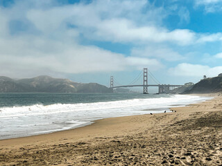 Coastal view of the Golden Gate bridge in San Francisco. American iconic landmark. Cliffs and grass frame the picture. Waves in the bay water. Light fog.