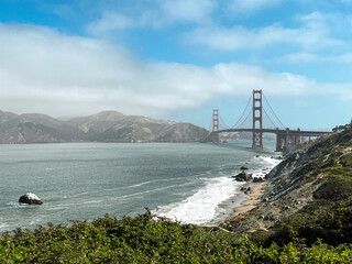 Coastal view of the Golden Gate bridge in San Francisco. American iconic landmark. Cliffs and grass frame the picture. Waves in the bay water. Light fog.