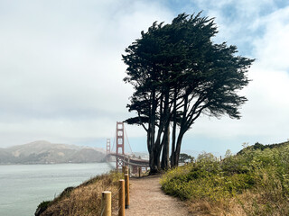 Coastal view of the Golden Gate bridge in San Francisco. American iconic landmark. Cliffs and grass frame the picture. Waves in the bay water. Light fog.