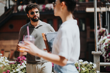 Group of colleagues engaged in a casual business meeting outdoors, enjoying refreshing drinks in a sunny garden setting with flowers and greenery.