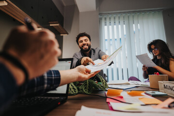 In a lively office environment, a group of diverse colleagues energetically discusses business projects and solutions, sharing paperwork and ideas.
