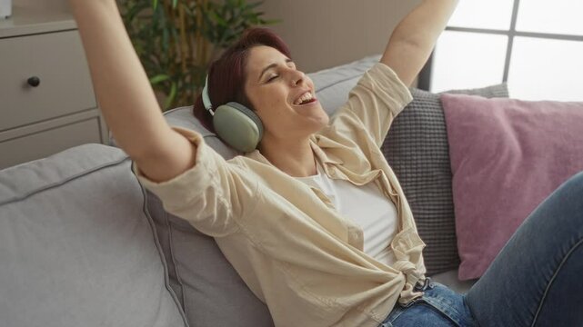 Young woman with short hair enjoying music with headphones on a sofa at home.