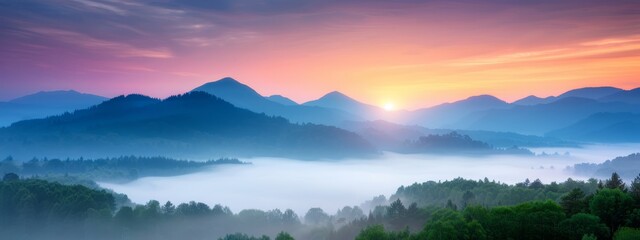 Fototapeta premium The sun sets over mist-covered mountains, trees line the distant horizon