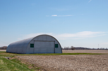 A half round barn in a corn field.