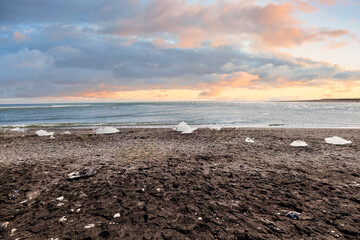 Sunset at Diamond Beach in Iceland with shimmering ice chunks on the black sand shoreline