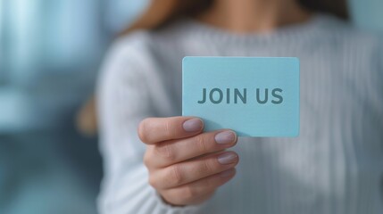 Close-up of a person holding a blue card with 'Join Us' text, inviting participation or membership.