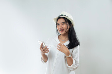 Beautiful young Asian woman tourist in straw hat standing posing with hand holding her smart phone and pointing, woman advertising online purchase