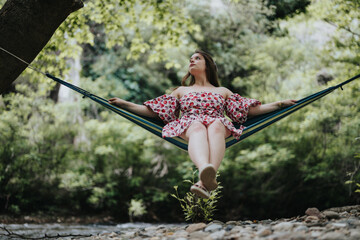 A woman in a floral dress enjoys a relaxing moment in a hammock, surrounded by lush greenery in a forest during summer.