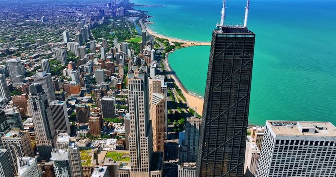 Dark skyscraper of the John Hancock Center towering above the gorgeous cityscape. Drone footage above the Lakeshore Drive approaching waterscape of Lake Michigan on sunny day.