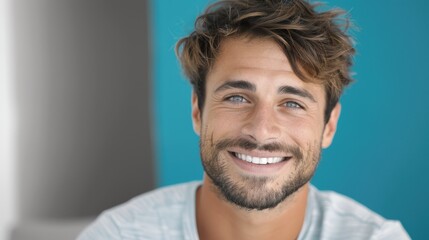 Fototapeta premium Young man smiling brightly at the camera against a turquoise backdrop, conveying happiness and positivity in a casual setting, captured with a vivid and fresh aesthetic.