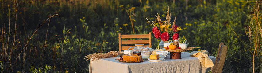 Elegant countryside table setting outdoor in the garden. White porcelain cups, teapot with herbal tea, homemade pumpkin spicy sweet pie. Family tradition, beautiful place outside. Fall mood. Banner