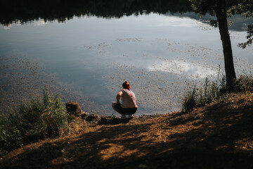 Fototapeta premium Individual crouching by a serene lake, encapsulating the essence of solitude and relaxation in nature